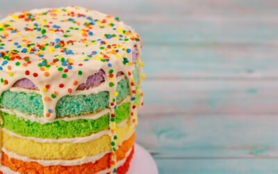 Gâteau arc-en-ciel à partager avec des amis, décoré de bonbons et de paillettes.